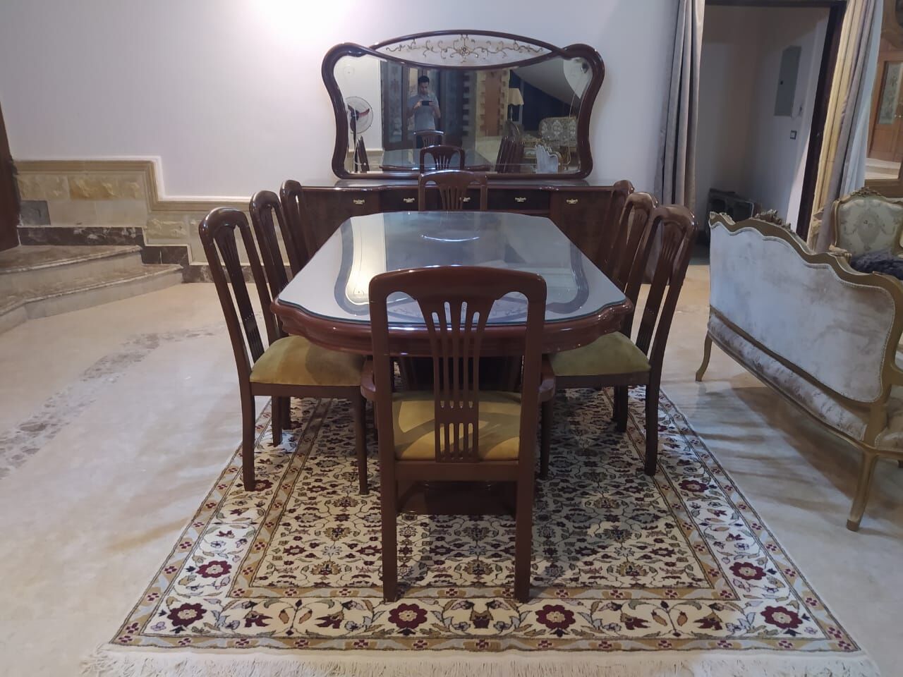 Wooden dining table and chairs with a mirrored cabinet behind, on a floral cream rug