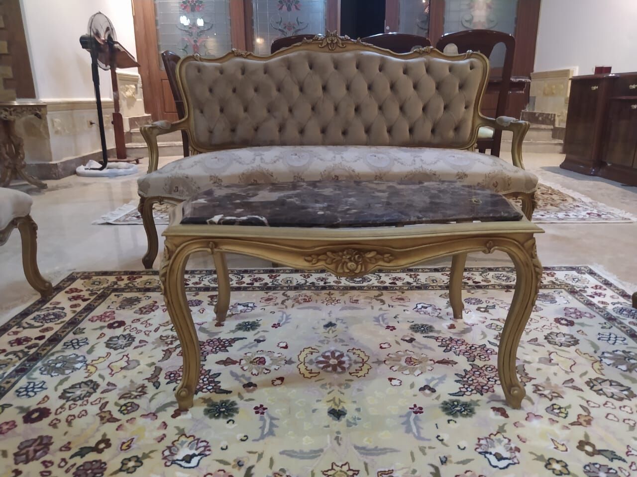 Gilded-frame sofa and marble coffee table on a cream floral rug with a navy border