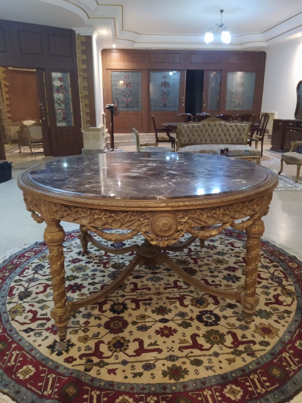 Ornate gilded round table on a round rug with a red and navy border