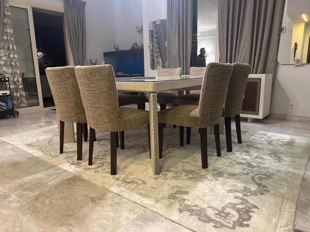 Dining table and upholstered chairs on a cream rug with a grey scrolling pattern