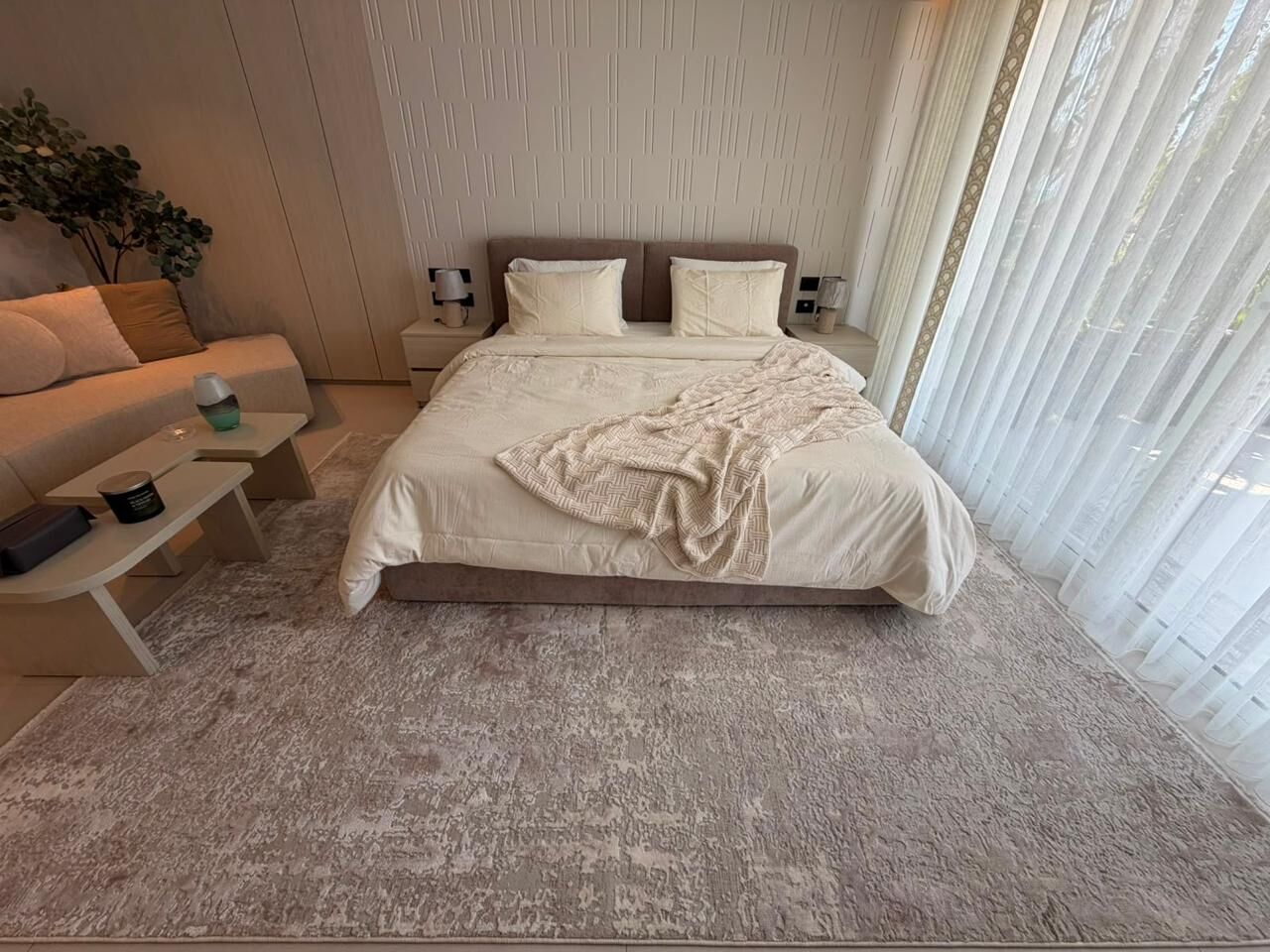 Bed with white bedding on a mauve-grey rug, with a sofa at the side