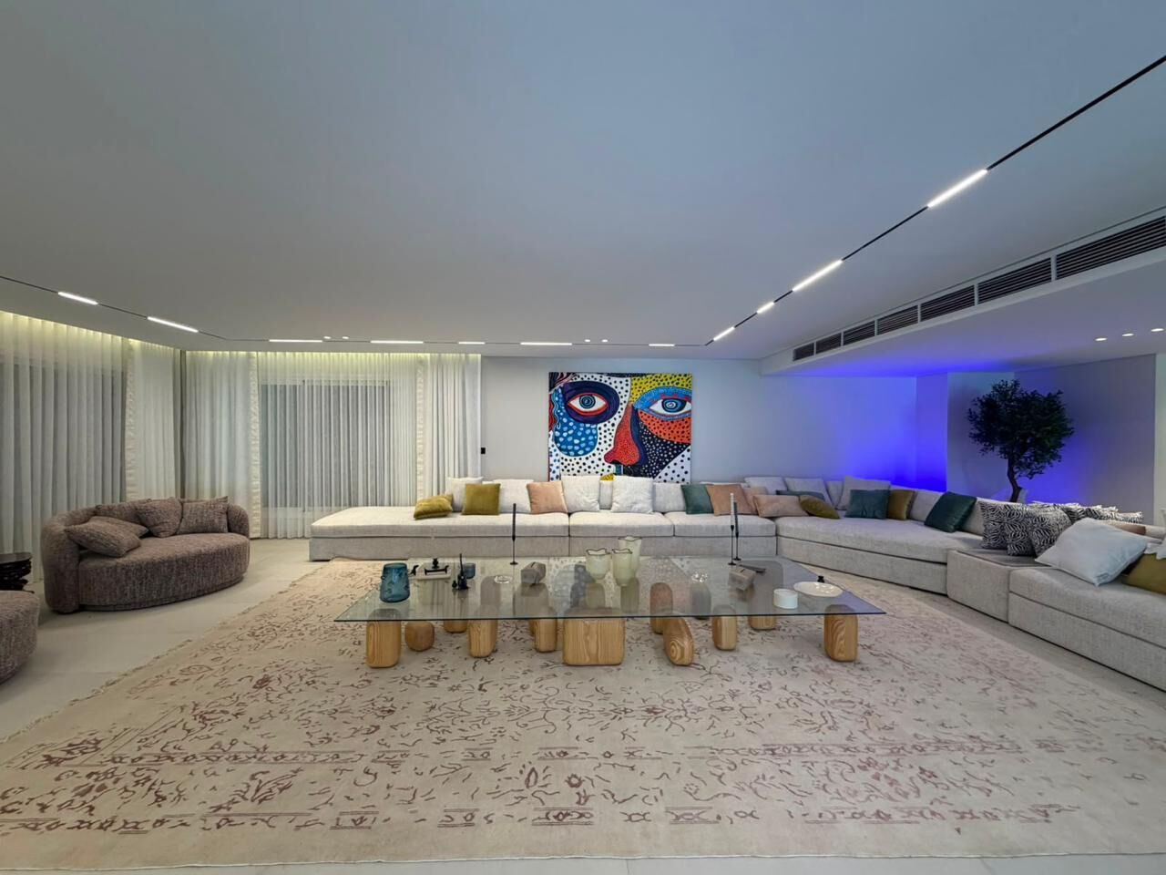 Wide living room with a long sofa, a colourful painting and a glass coffee table on a pale rug