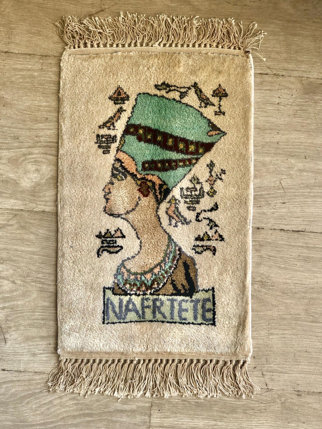 Small pictorial pile rug showing a profile bust of a queen in a green crown, with hieroglyph-style symbols and fringed ends