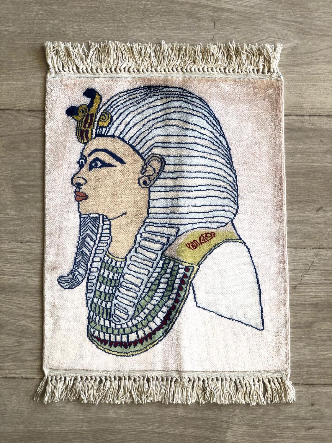 Small pictorial rug showing the head of a pharaoh in a striped headdress and layered collar, on a pale pink field